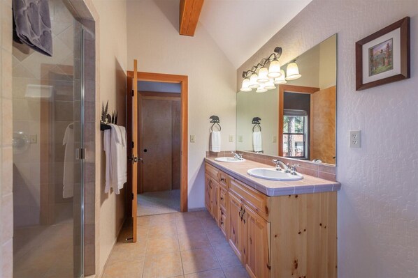 Un baño con cabina de ducha de vidrio, muebles de madera, un espejo grande y una ventana.