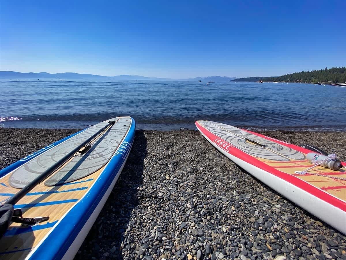 Two paddleboards on a pebbled beach with a clear view of the water and distant mountains.