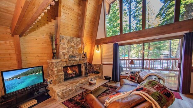A cozy cabin interior with a stone fireplace, leather sofa, and a television displaying a scenic view. - Evans Cabin (Carnelian Bay)
