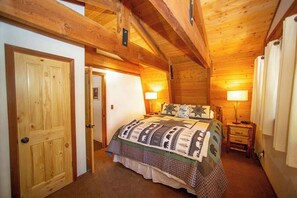 A wooden-paneled bedroom with a bed, two bedside lamps, and a door. - Evans Cabin (Carnelian Bay)