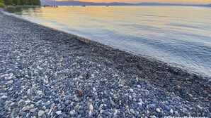A pebbled beach with calm water and distant boats. - Evans Cabin (Carnelian Bay)