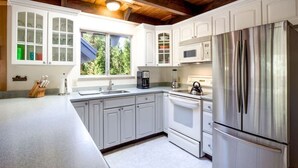 A modern kitchen with white cabinetry, stainless steel appliances, and a window providing natural light. - O`Rourke Cabin, 4BD/2BA (Carnelian Bay)