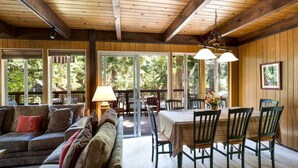 A cozy interior with a wooden ceiling, a sofa set, a dining table with chairs, and large windows offering a view of greenery. - O`Rourke Cabin, 4BD/2BA (Carnelian Bay)