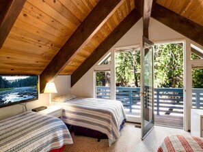 A bedroom with two beds, a TV, and a balcony with a view of trees. - O`Rourke Cabin, 4BD/2BA (Carnelian Bay)