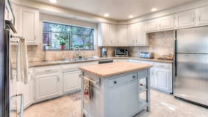 A modern kitchen with white cabinets, a stainless steel refrigerator, and a large window providing natural light.