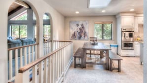 A spacious kitchen with modern appliances, a dining area with a wooden table, and a view through an arched window.