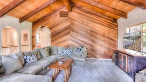 A cozy living room with a wooden ceiling, a sectional sofa, a coffee table, and a TV.
