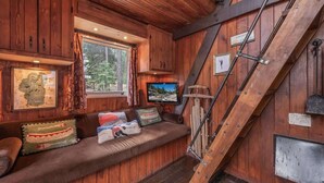 A cabin interior with a wooden wall, a built-in bench with cushions, a television, and a metal staircase. - Sunshine Cabin (Carnelian Bay)