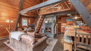 A rustic cabin interior with a loft bedroom, a fireplace, wooden furniture, and a dining area. - Sunshine Cabin (Carnelian Bay)