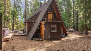 A cabin with a steeply pitched roof, wooden exterior, and a deck area with outdoor seating. - Sunshine Cabin (Carnelian Bay)
