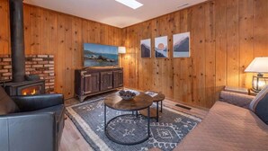 A cozy room with a fireplace, wooden walls, a sofa, a table, and framed pictures. - Triple C, Private Hot Tub, Dog-Friendly (Carnelian Bay)
