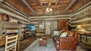 Interior rústico de una cabaña de troncos con una mesa de comedor de madera, sofá de cuero y una chimenea.