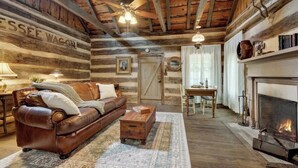 Interior rústico de una cabaña de troncos, con un sofá de cuero, una mesa de centro de madera, chimenea y un comedor.