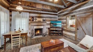 Interior rústico de una cabaña con chimenea, mesa de comedor de madera y zona de estar acogedora.