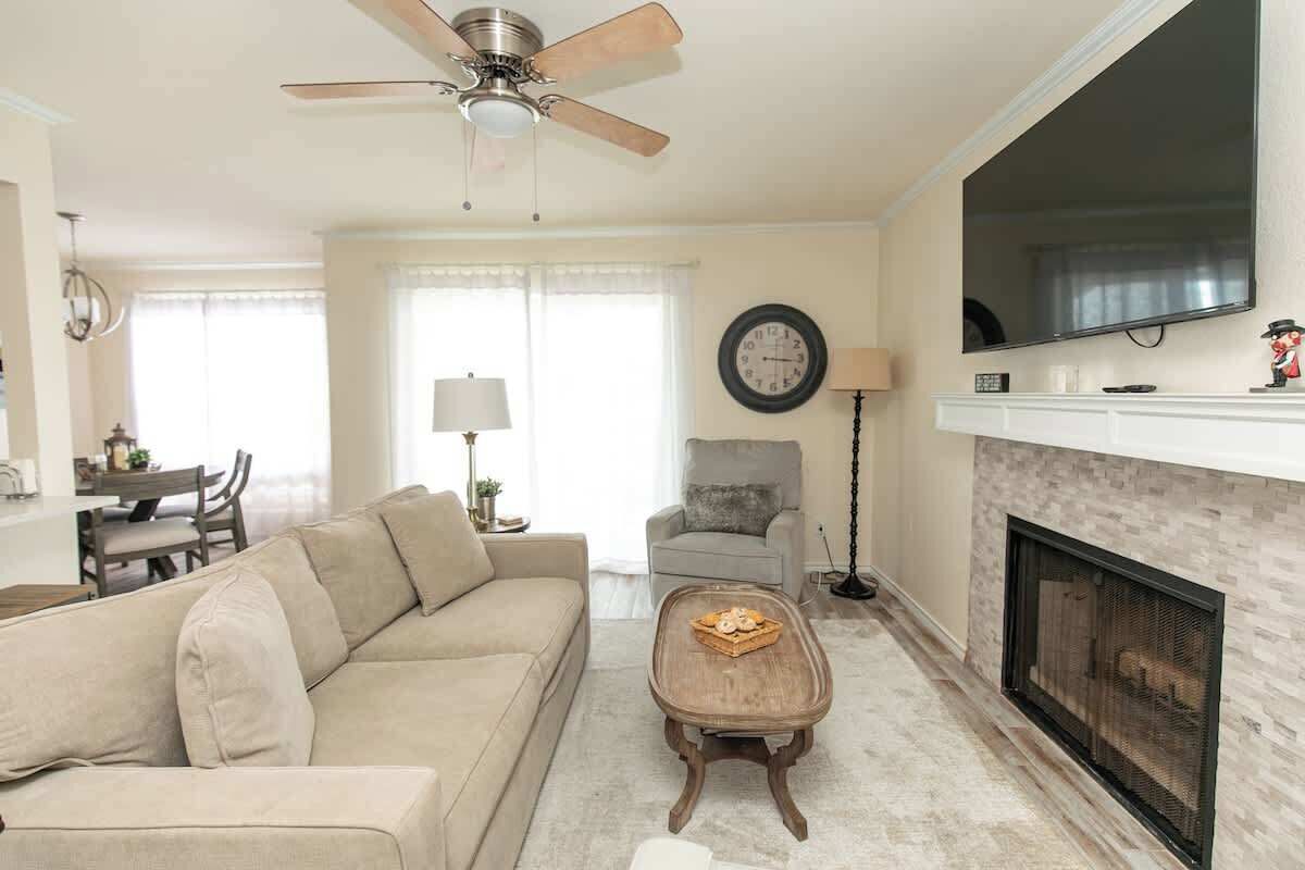 A living room with a sofa, a coffee table, a fireplace, a television, and a ceiling fan.