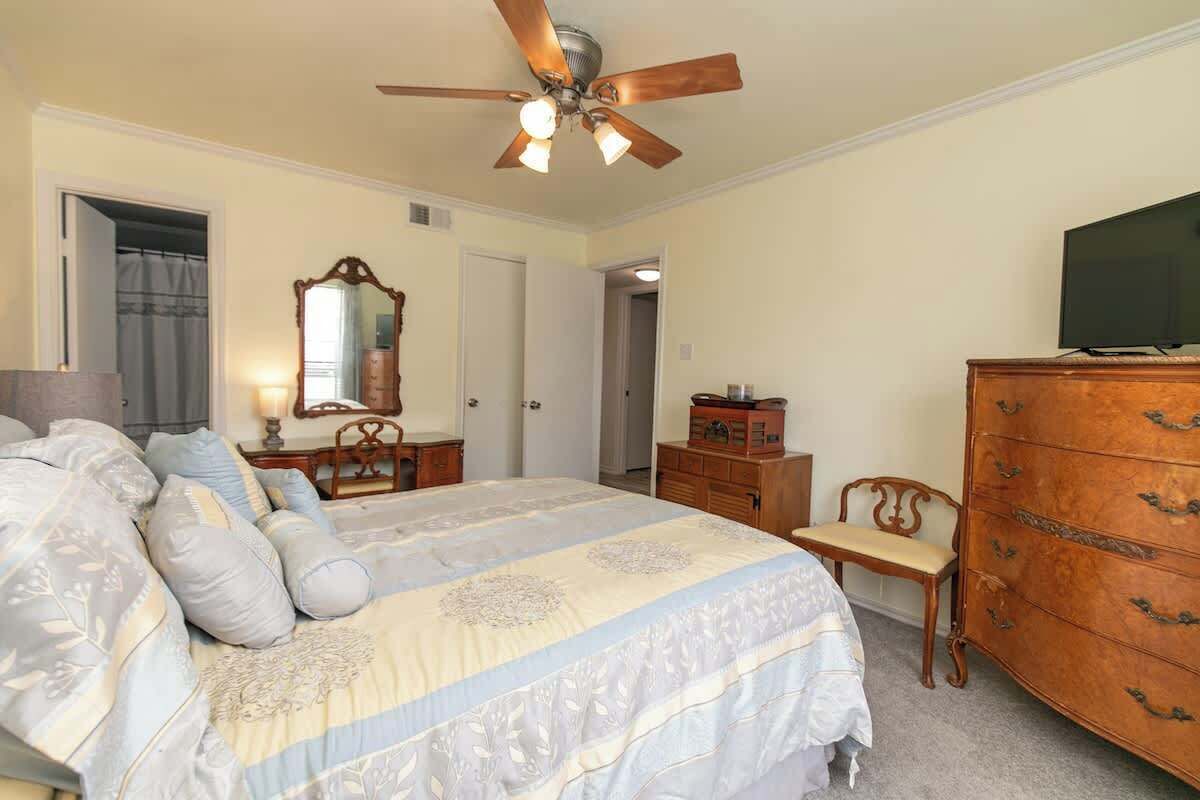 Un dormitorio con cama, cómoda, televisor, ventilador de techo y espejo.