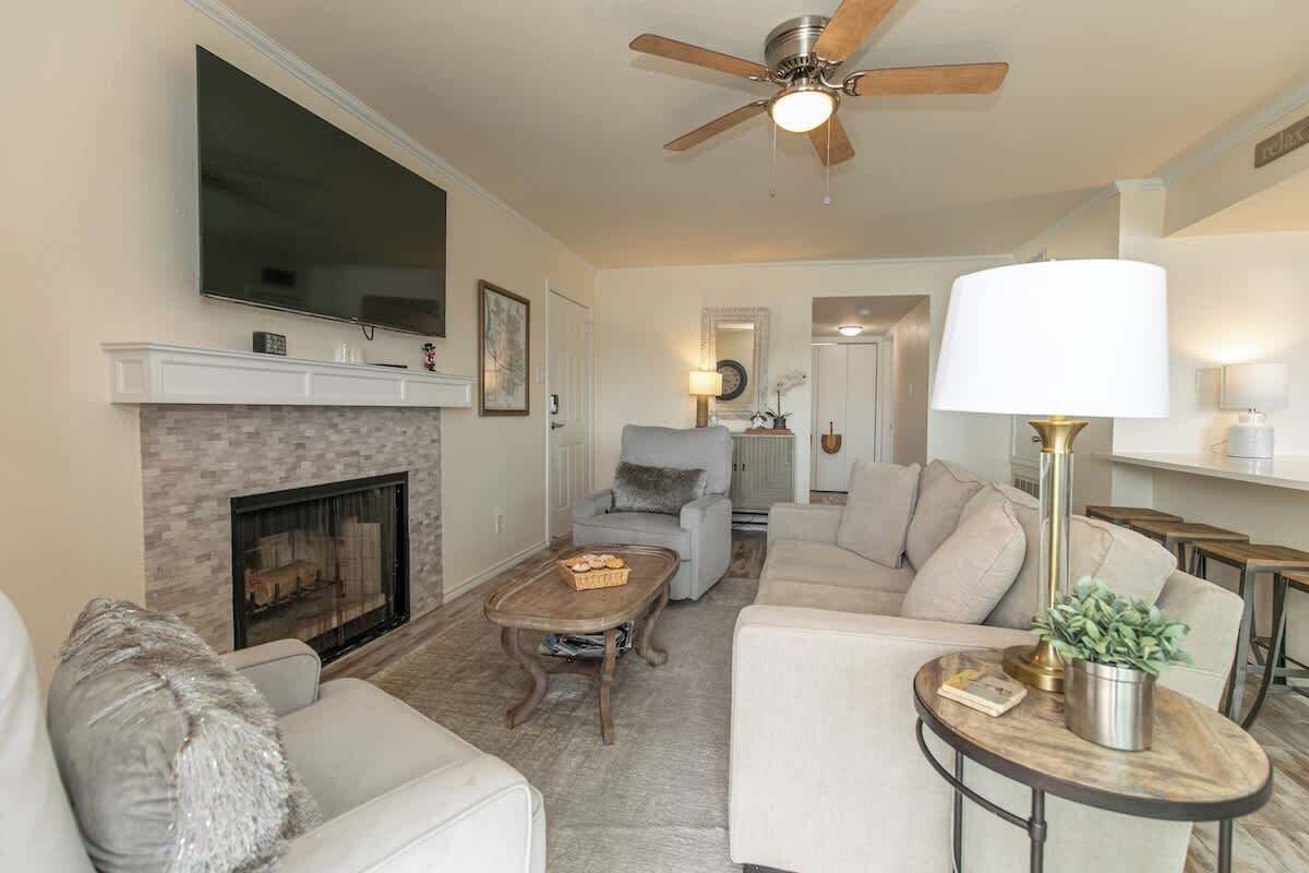 A living room with a fireplace, a ceiling fan, a television, and a dining area.