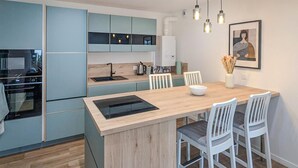A modern kitchen with light blue cabinets, a wooden island, white chairs, and a dining table. - 1 bedroom beautiful apartment in Gagny (Gagny)