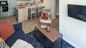A modern living room with a sofa, a coffee table, and a TV. There is a kitchen in the background with a dining area. - 1 bedroom beautiful apartment in Gagny (Gagny)