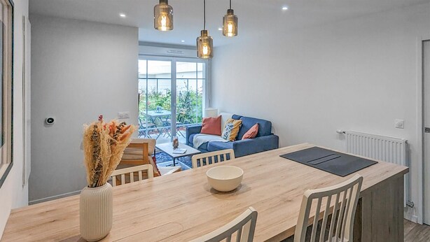 A modern kitchen with a wooden dining table, chairs, and pendant lights. A vase with dried flowers is on the table. - 1 bedroom beautiful apartment in Gagny (Gagny)