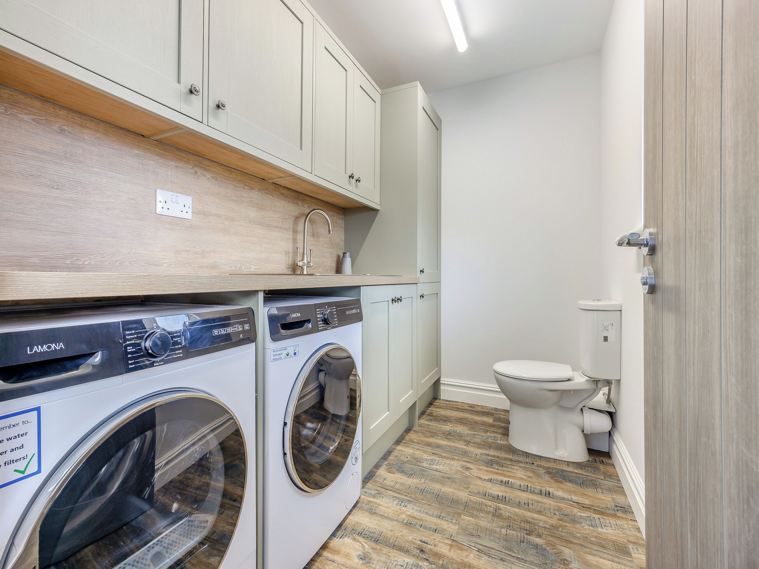 A laundry room with two front-loading washing machines, a wooden countertop, and a white toilet.