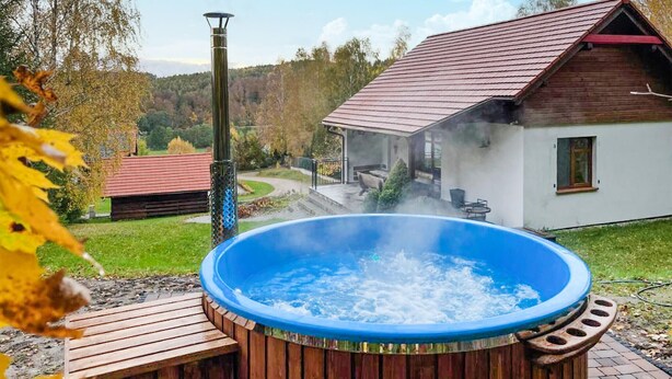 A hot tub with a wooden deck, a rustic house with a red roof, and a forested background. - 2 bedroom beautiful home in Krzeszna (Krzeszna)