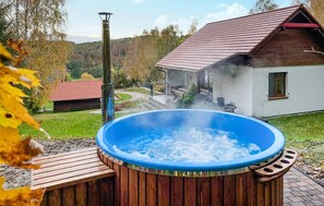A hot tub with a wooden deck, a rustic house with a red roof, and a forested background. - 2 bedroom beautiful home in Krzeszna (Krzeszna)