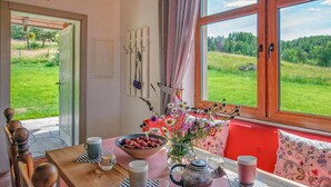 A dining area with a table set for two, a bowl of strawberries, a vase with flowers, and a view of a green landscape through large windows. - 2 bedroom beautiful home in Krzeszna (Krzeszna)
