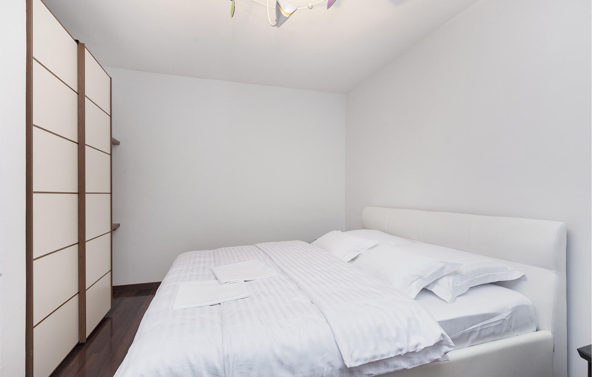 Een minimalistische slaapkamer met een bed, een kledingkast en een plafondlamp.