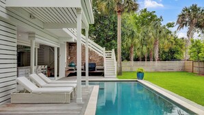 A poolside area with lounge chairs, a barbecue setup, and a brick wall. - Be a Sullivans Local! 1307 Cove Avenue by Avantstay Pool + Outdoor Living (Sullivan's Island)