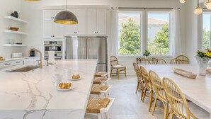 Een moderne keuken met witte kastjes, een groot eiland en een eethoek met rieten stoelen.