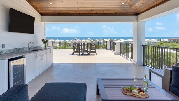Een moderne keuken met een grote televisie, een eethoek met een tafel en stoelen, en een balkon met uitzicht op zee.