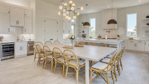 Een ruime keuken met witte kasten, een groot eiland en een eethoek met rieten stoelen.