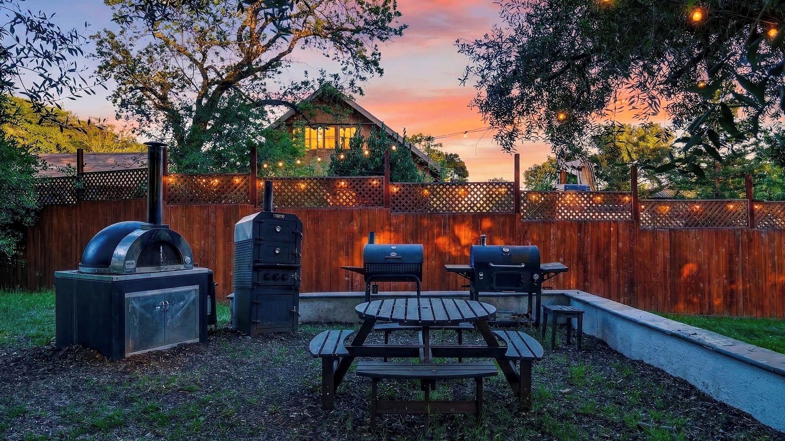 Un giardino attrezzato con barbecue, forno per pizza e tavolo con panche.