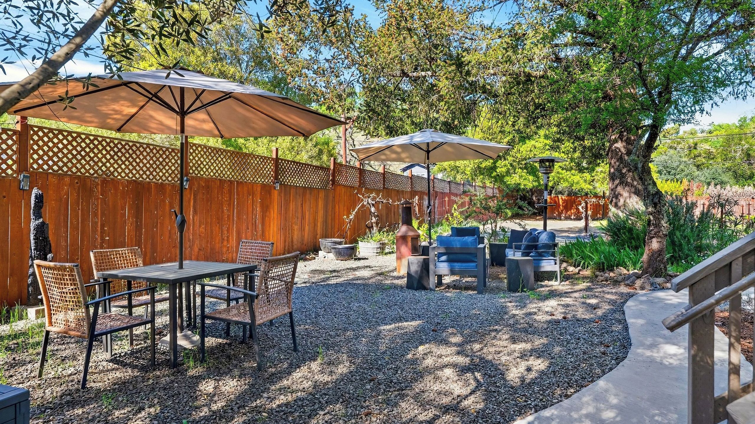 An outdoor patio with tables and chairs, umbrellas, and a barbecue grill.