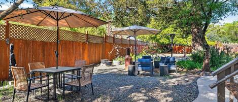An outdoor patio with tables and chairs, umbrellas, and a barbecue grill.