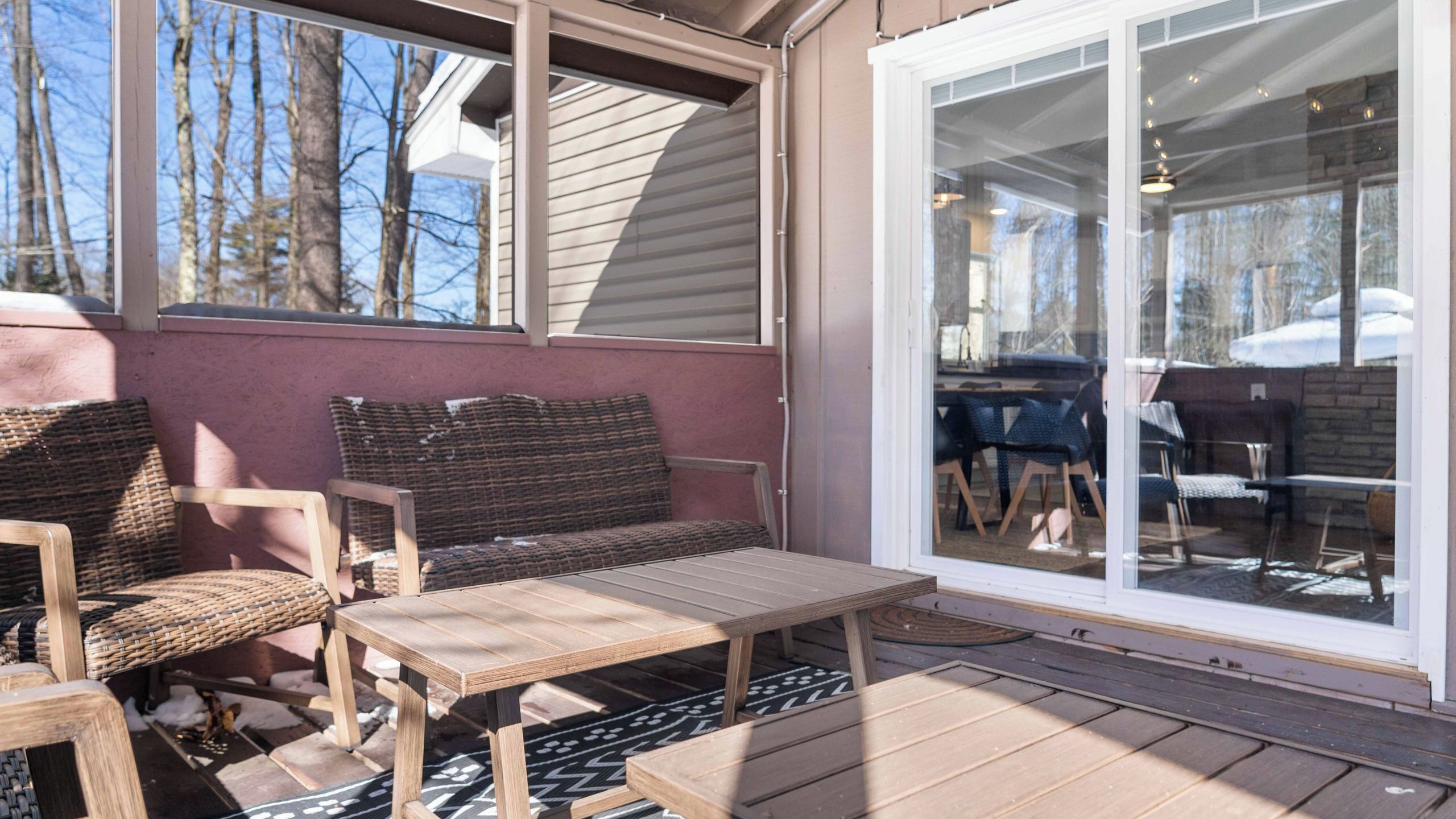 Een overdekt terras met een tafel en stoelen, een schuifpui en uitzicht op de omgeving.