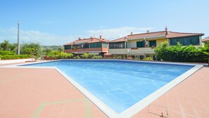 A swimming pool with a tiled deck, surrounded by houses with red-tiled roofs and a clear blue sky. - Lovely home in Pantai with WiFi (Pantai)