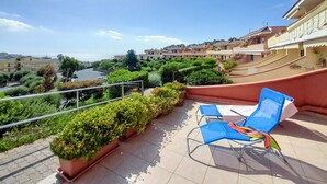 A balcony with blue lounge chairs, potted plants, and a view of a coastal area with buildings. - Lovely home in Pantai with WiFi (Pantai)