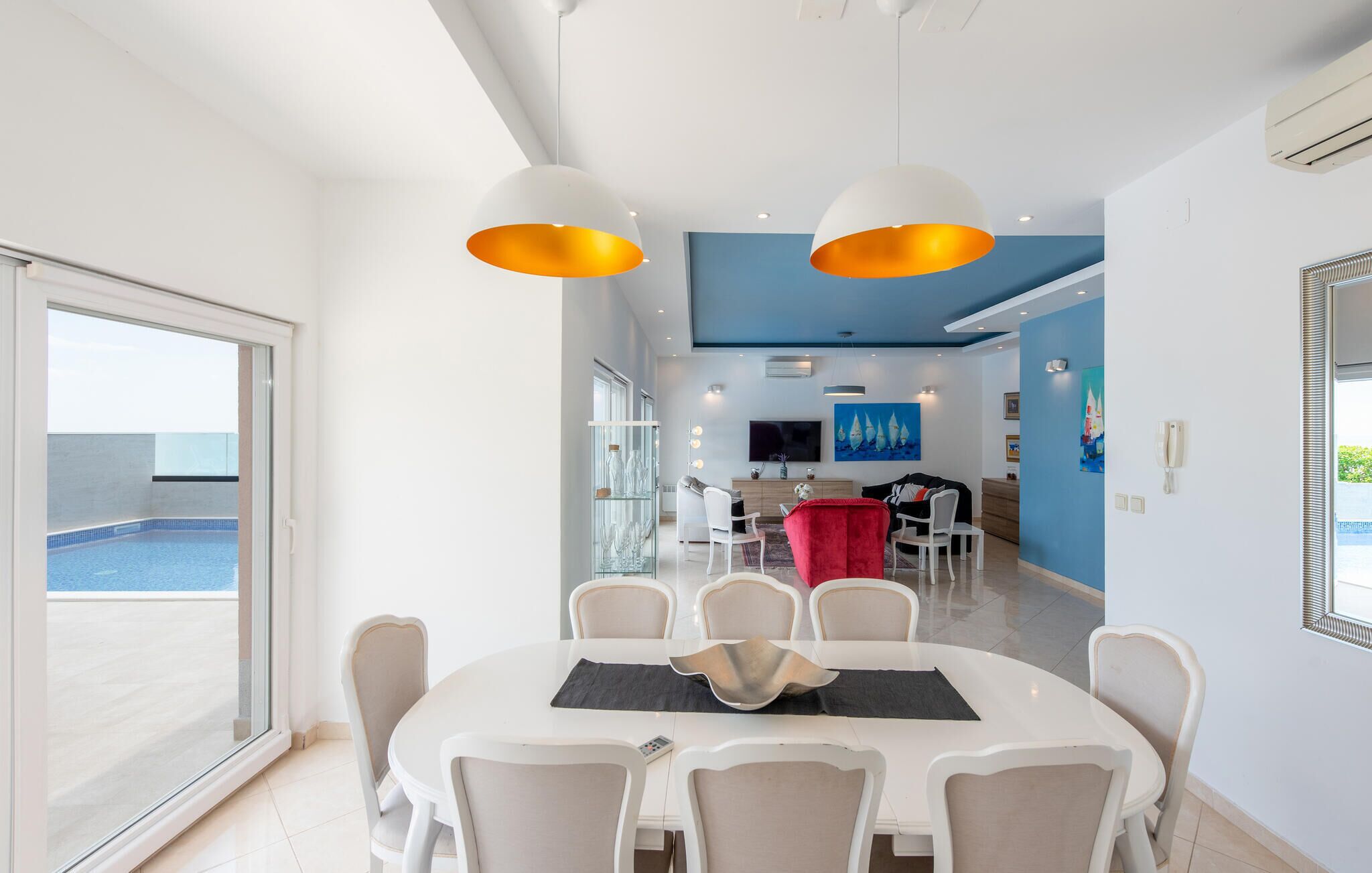Un espace de salle à manger moderne avec une table ronde, des chaises blanches et des luminaires suspendus.
