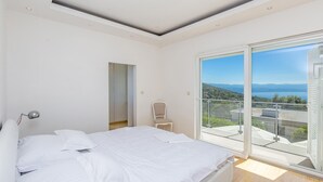 A bedroom with a bed, a chair, a mirror, and a large window with a view of a lake and mountains. - Stunning home in Poljane (Poljane)