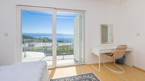 A modern bedroom with a large sliding glass door leading to a balcony, a white desk with a chair, and a bed with white bedding. - Stunning home in Poljane (Poljane)