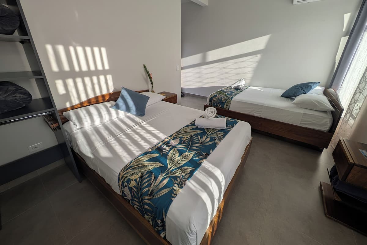 A hotel room with two beds, a wardrobe, a shelf, and an air conditioning unit.