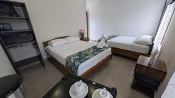 A hotel room with two beds, a small table with tea sets, a shelf with towels, and an air conditioning unit.