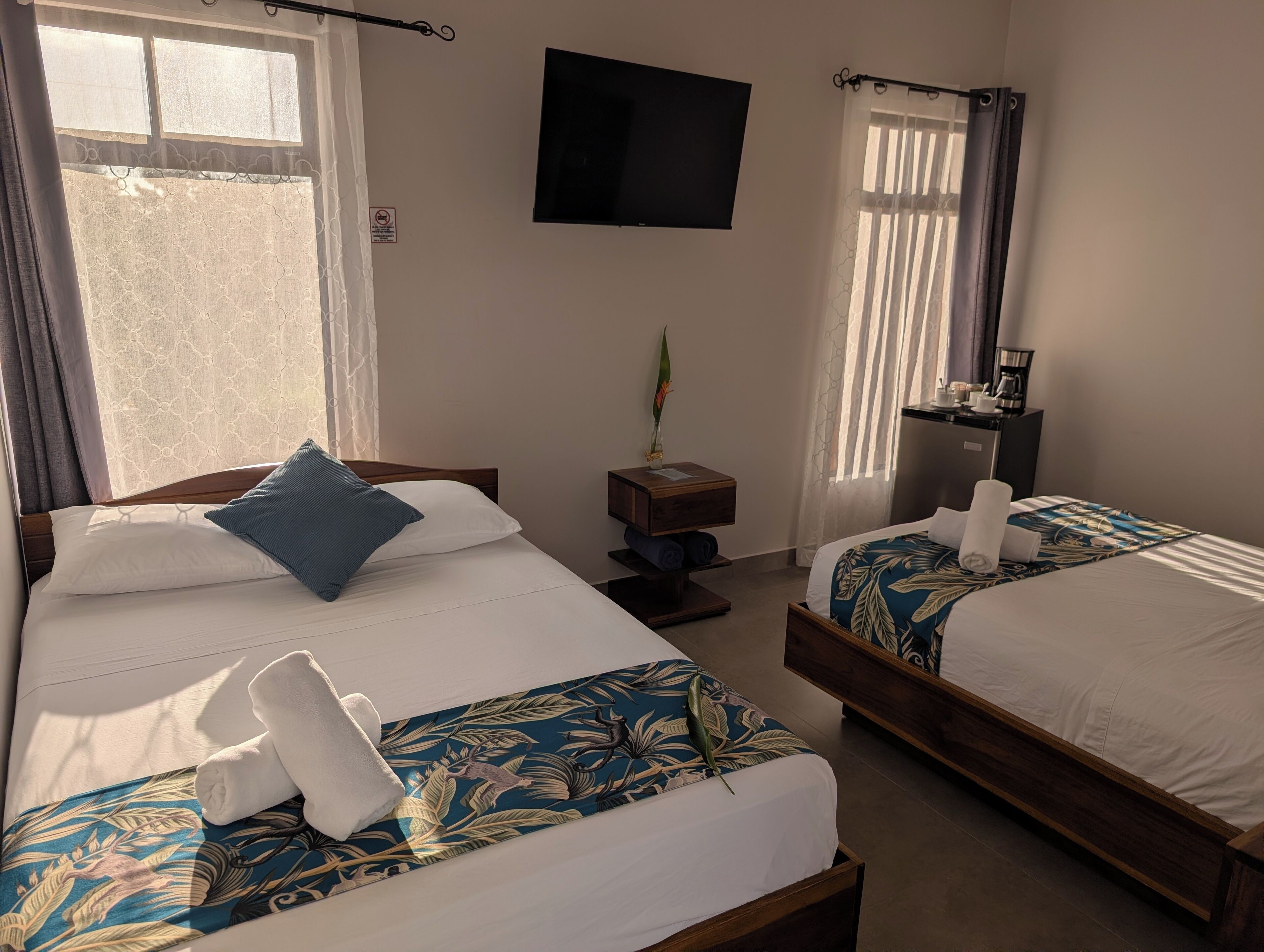A hotel room with two beds, a flat-screen TV, a nightstand, and a window with curtains.