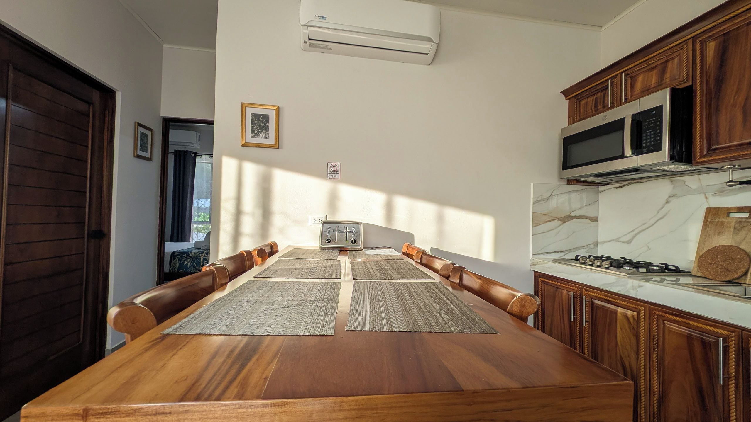A dining area with a wooden table, multiple chairs, a toaster, and a kitchen with a microwave and stove.