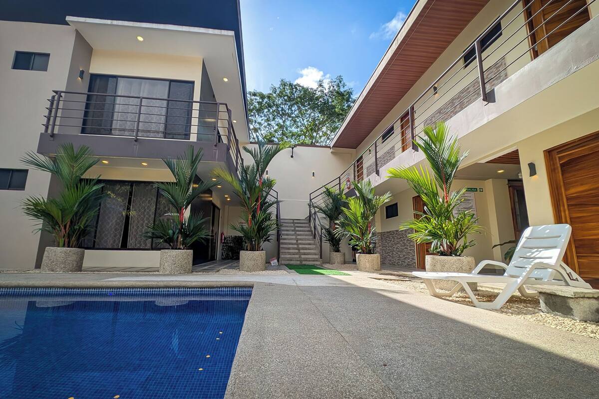 A modern building with a swimming pool, outdoor seating, and potted plants.