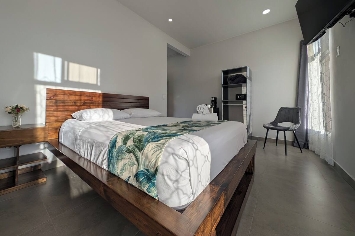 A modern hotel room with a wooden bed frame, a bedside table with a vase, a chair, and a built-in wardrobe.