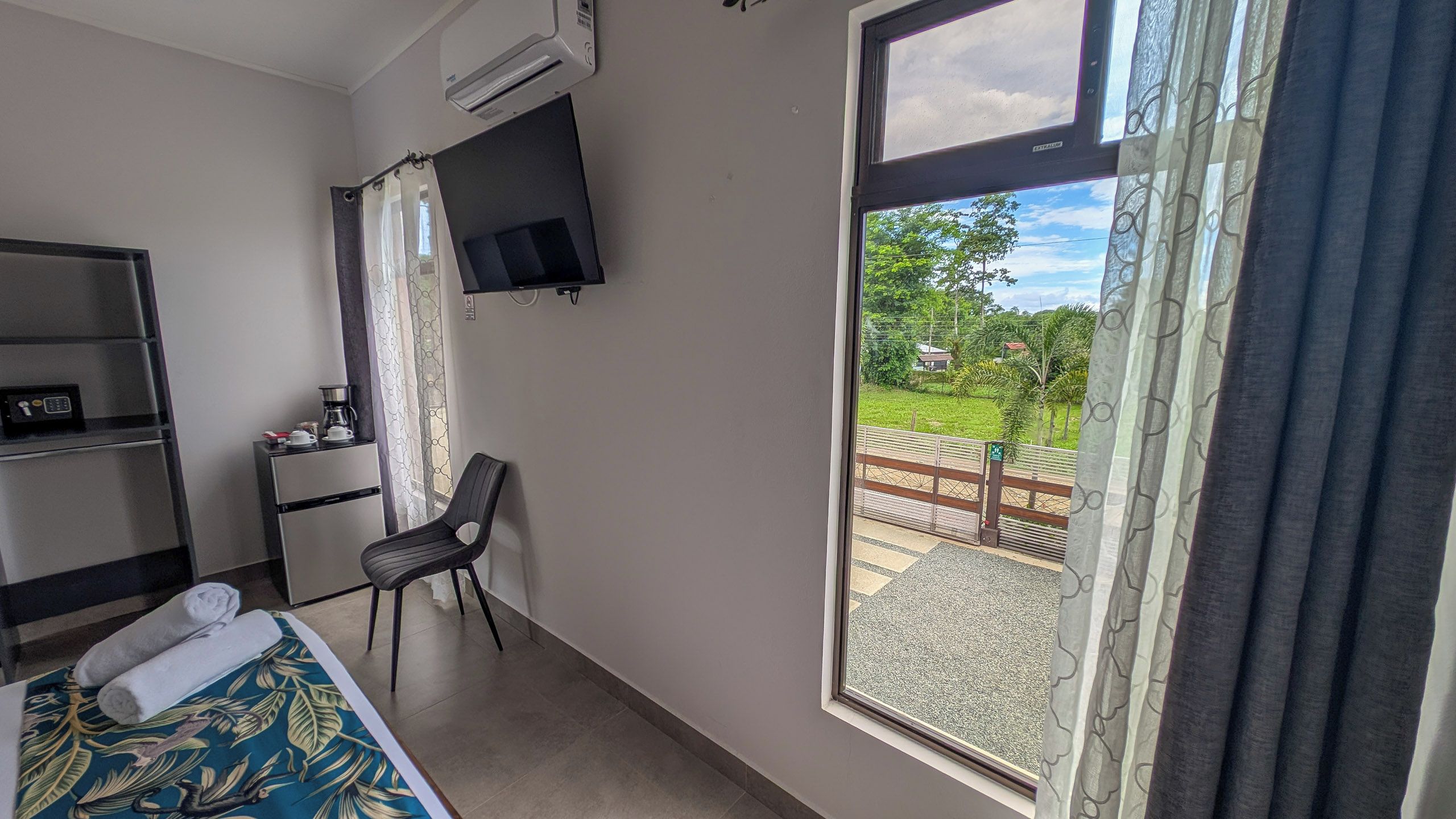 A hotel room with a bed, a desk with a chair, a TV mounted on the wall, and a window with a view of the outdoors.