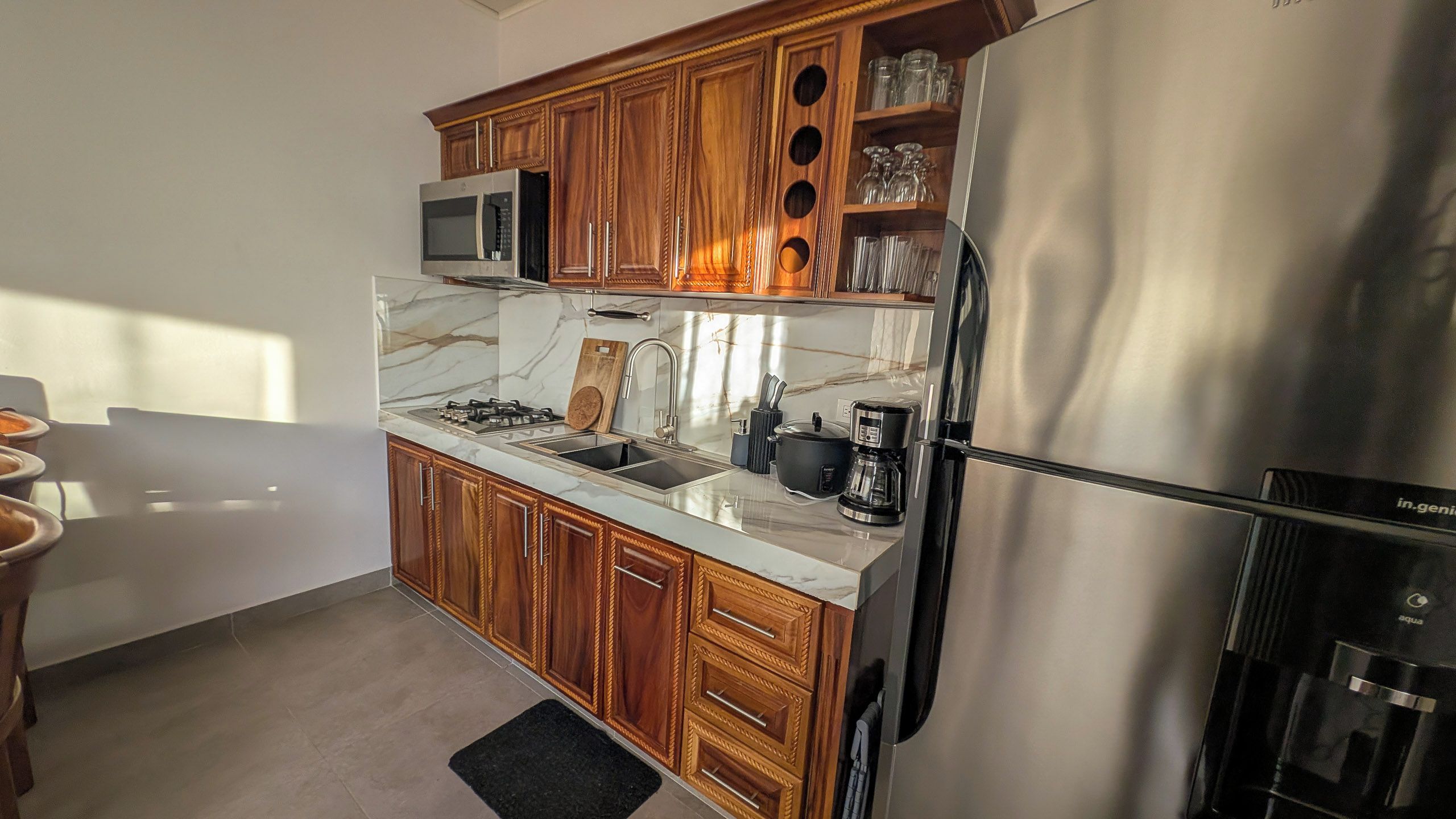 A compact kitchen with wooden cabinets, a stainless steel refrigerator, a microwave, and a coffee maker.